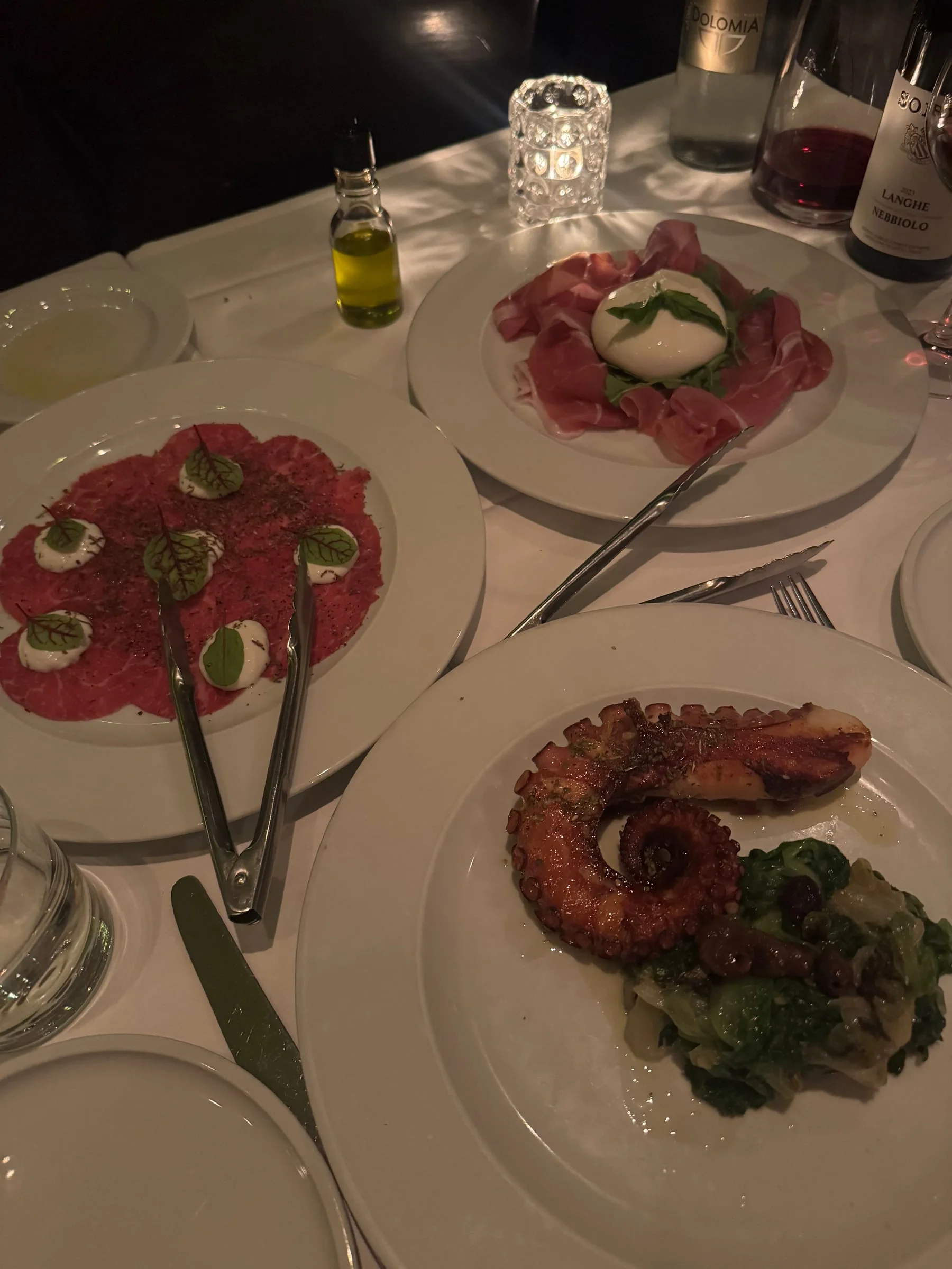 Beef carpaccio with stracciatella, grilled octopus, and prosciutto with burrata on a white tablecloth