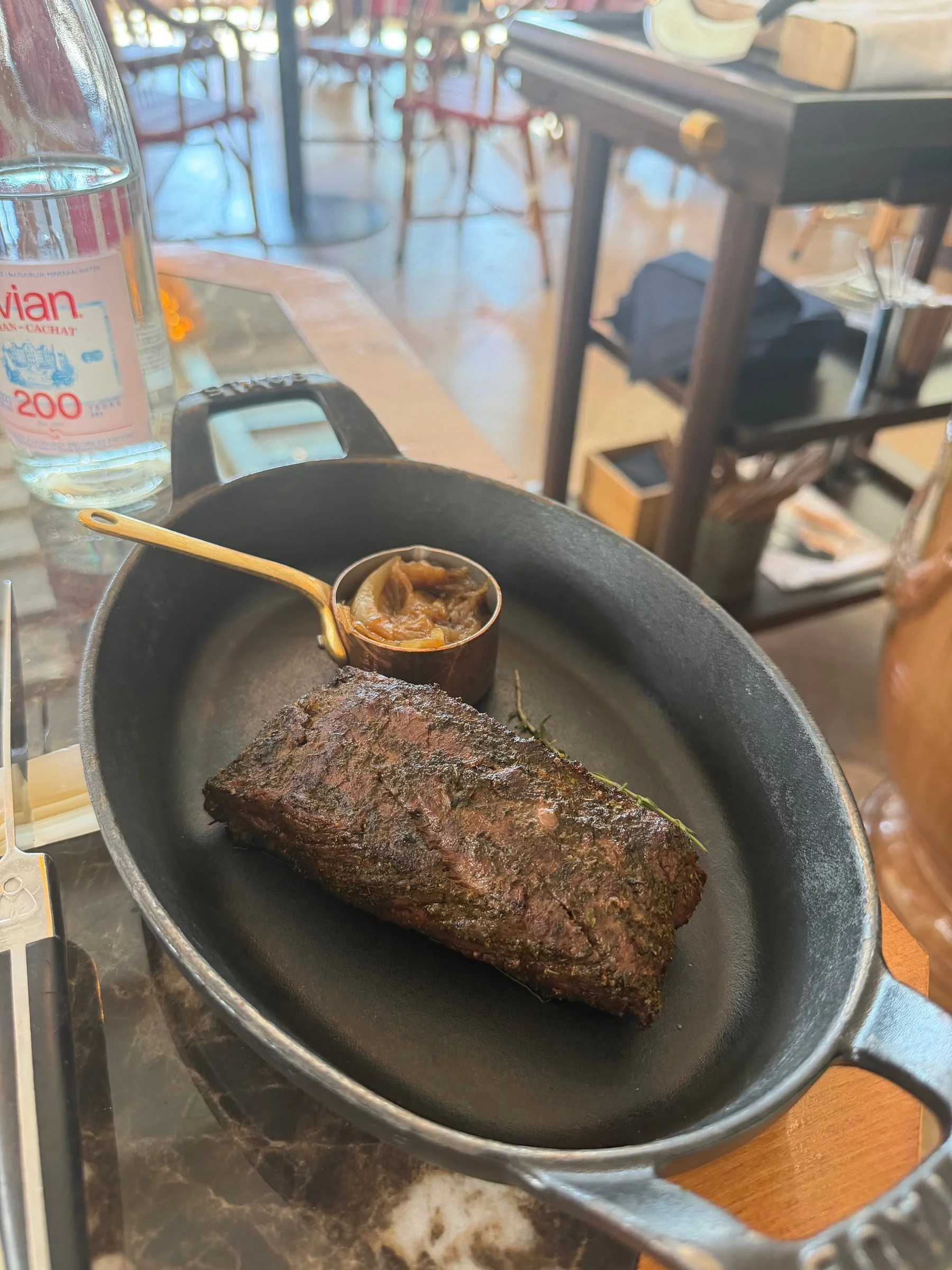 A rare bavette steak in a black cast-iron dish, with a small pot of sauce