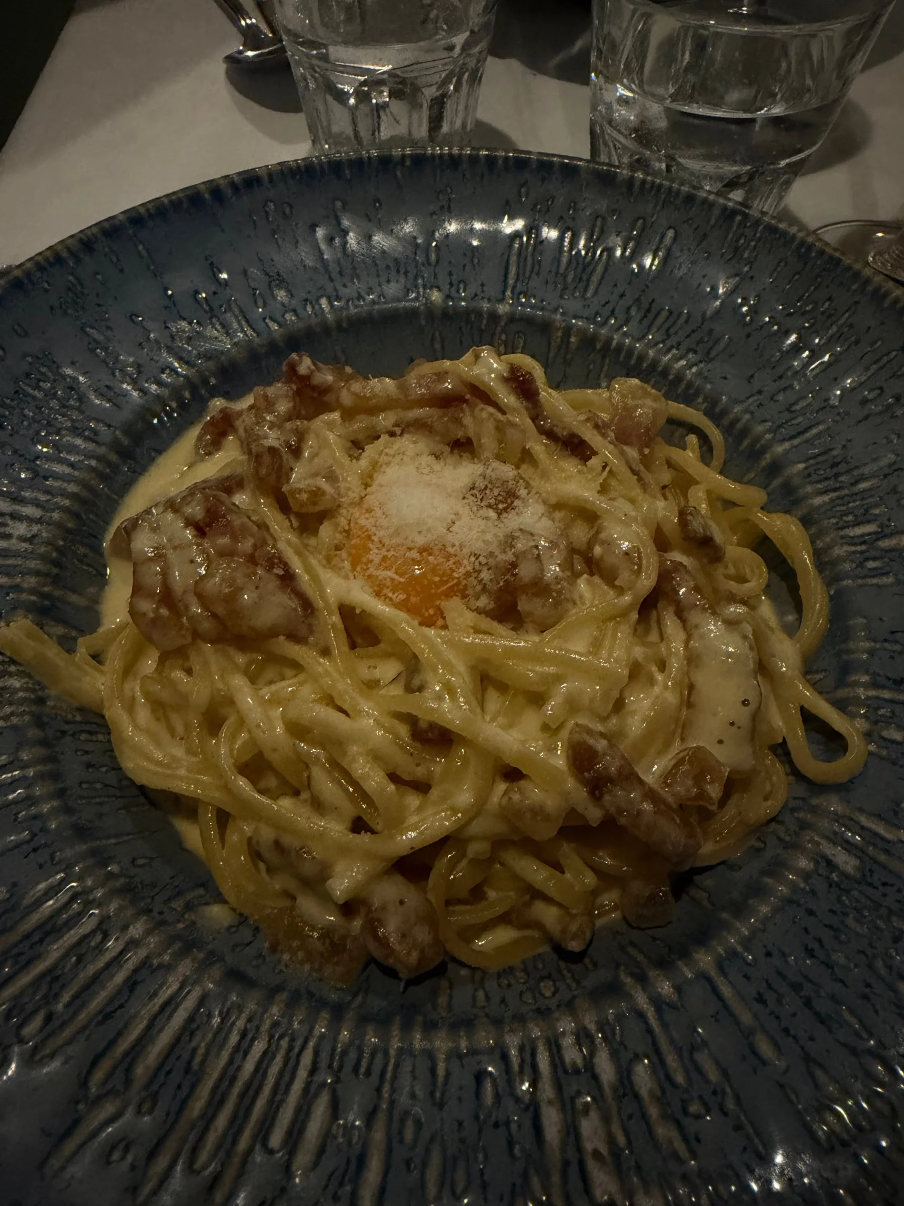 Spaghetti carbonara with lardons and a whole raw egg yolk on top, in a blue bowl