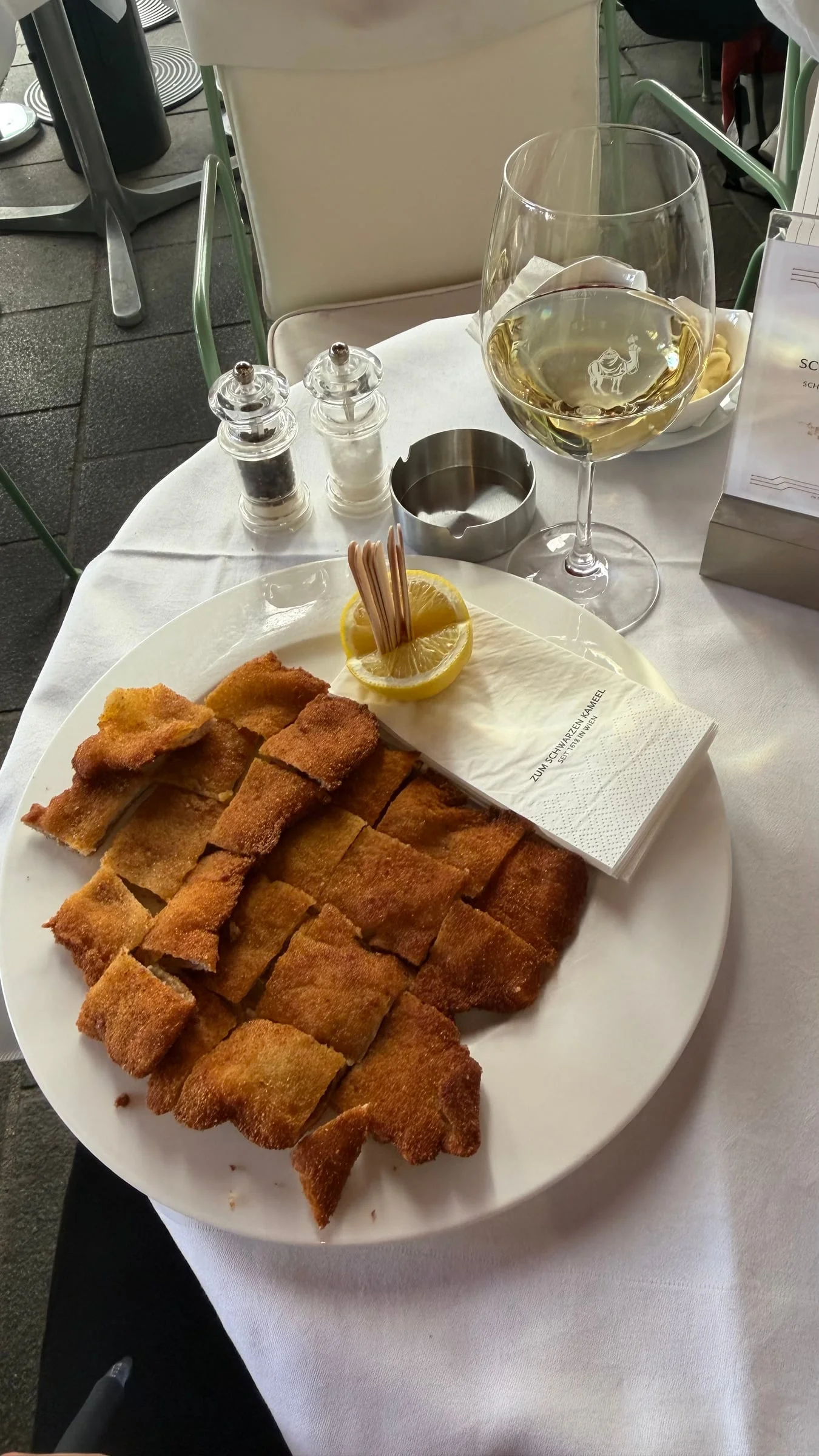 Wiener schnitzel cut into golden pieces, with lemon, on a white plate next to a glass of white wine